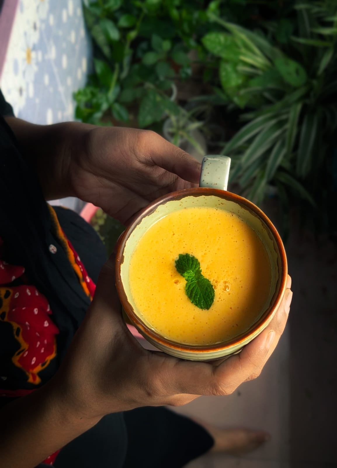 Hands holding a cup of mango juice garnished with mint