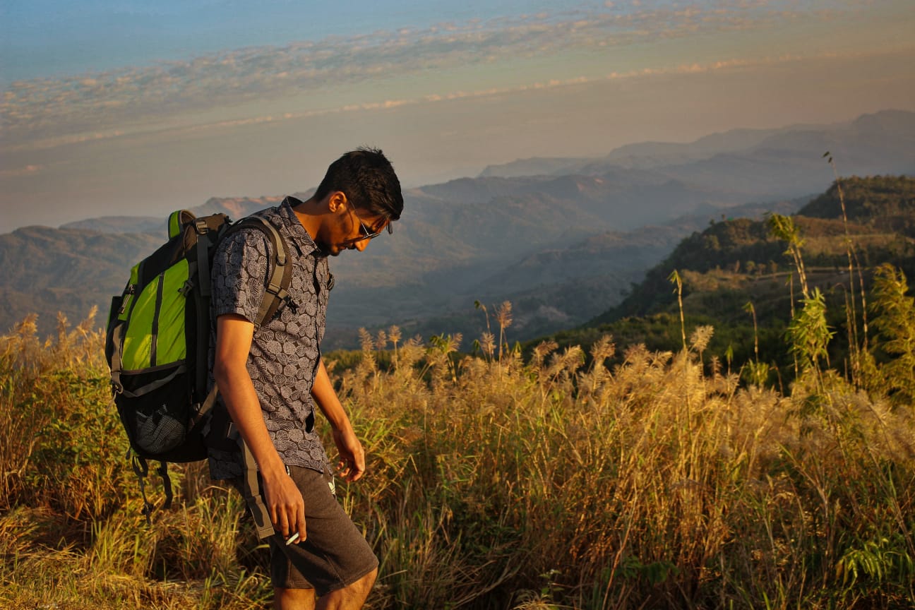 Hiker with a backpack walking a grassy ridge at sunset